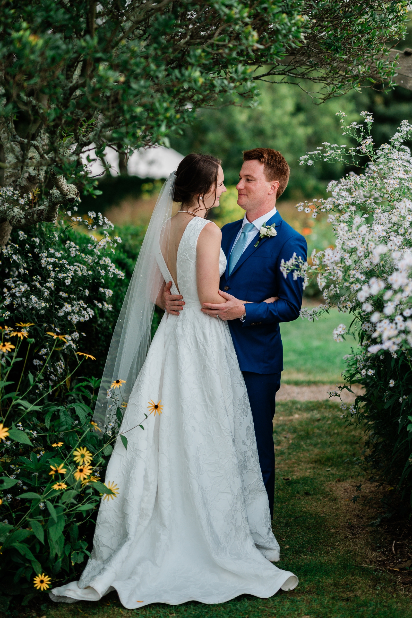 A couple poses amid blooming flowers at an outdoor wedding venue in New England
