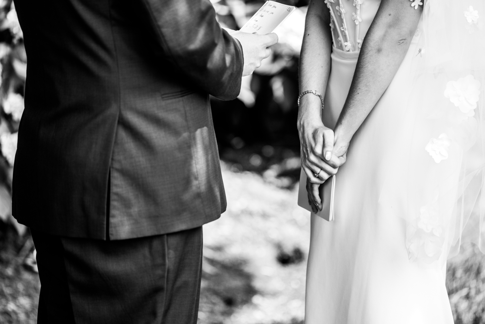 An intimate, black and white portrait of the bride and groom's hands holding their handwritten vow booklets