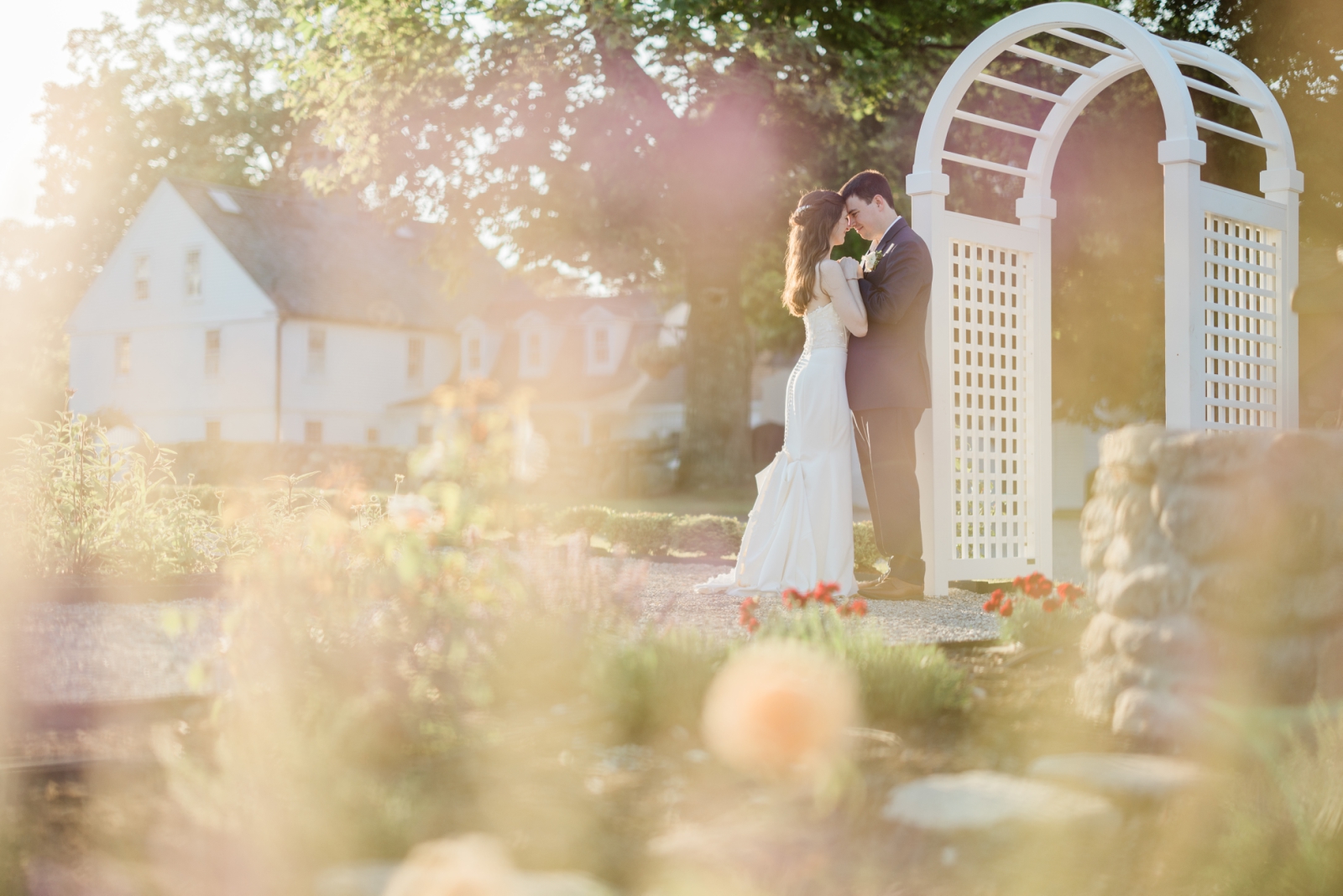 A bride and groom stand beneath a white arbor at Smith Farm Gardens
