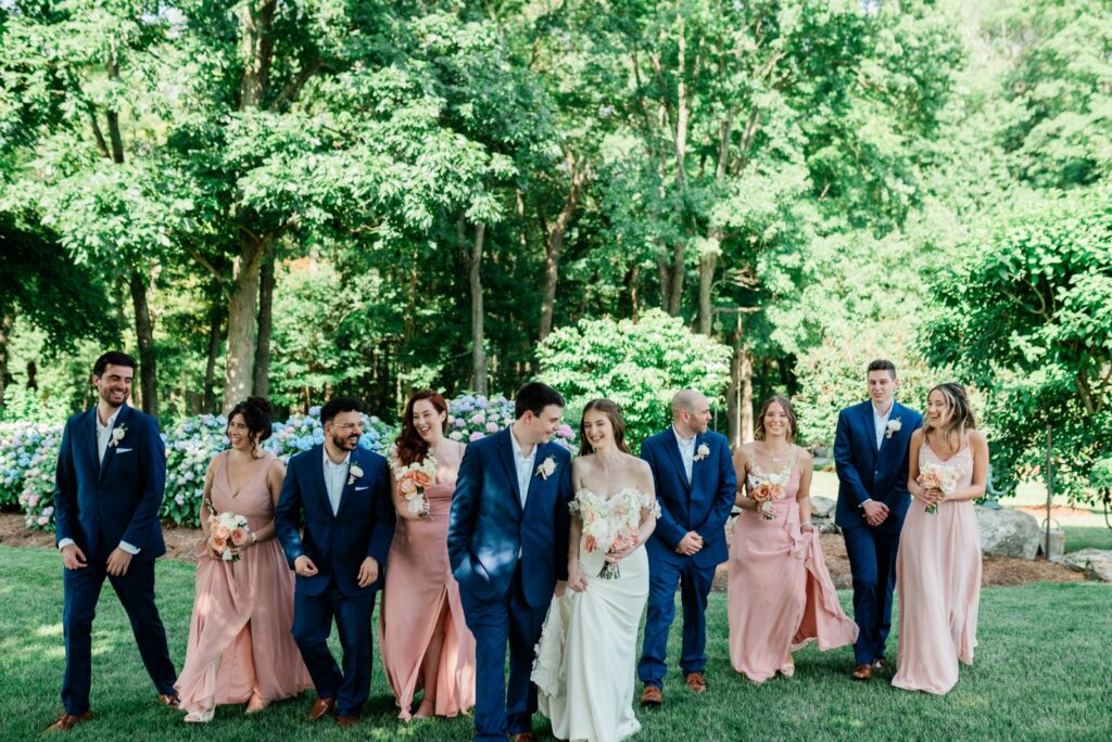 A wedding party wearing blush pink bridesmaids dresses and blue suits