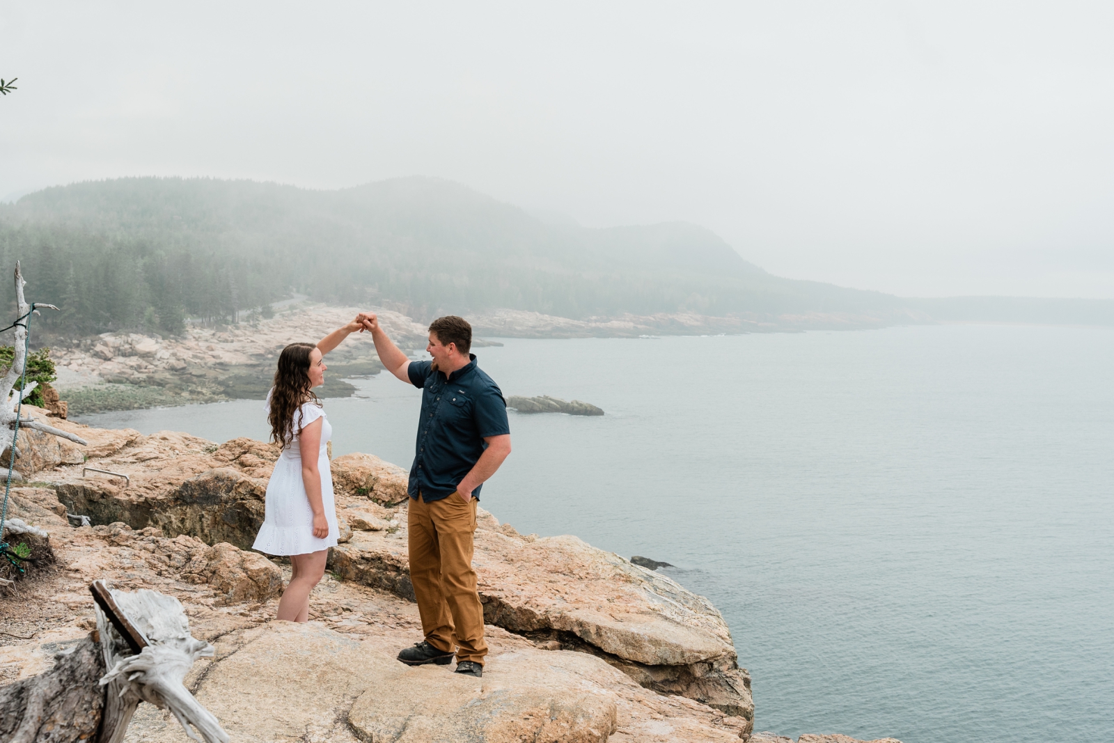 A man twirls a woman during engagement photos overlooking the ocean at Acadia National Park