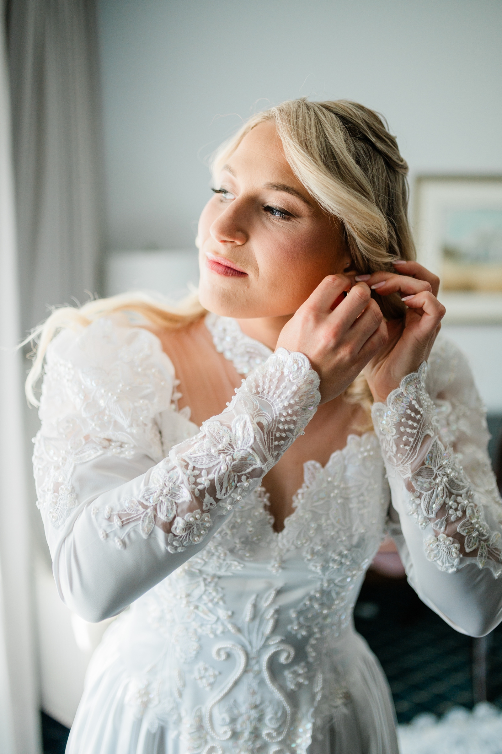 A bride wearing a wedding heirloom gown puts on her earrings