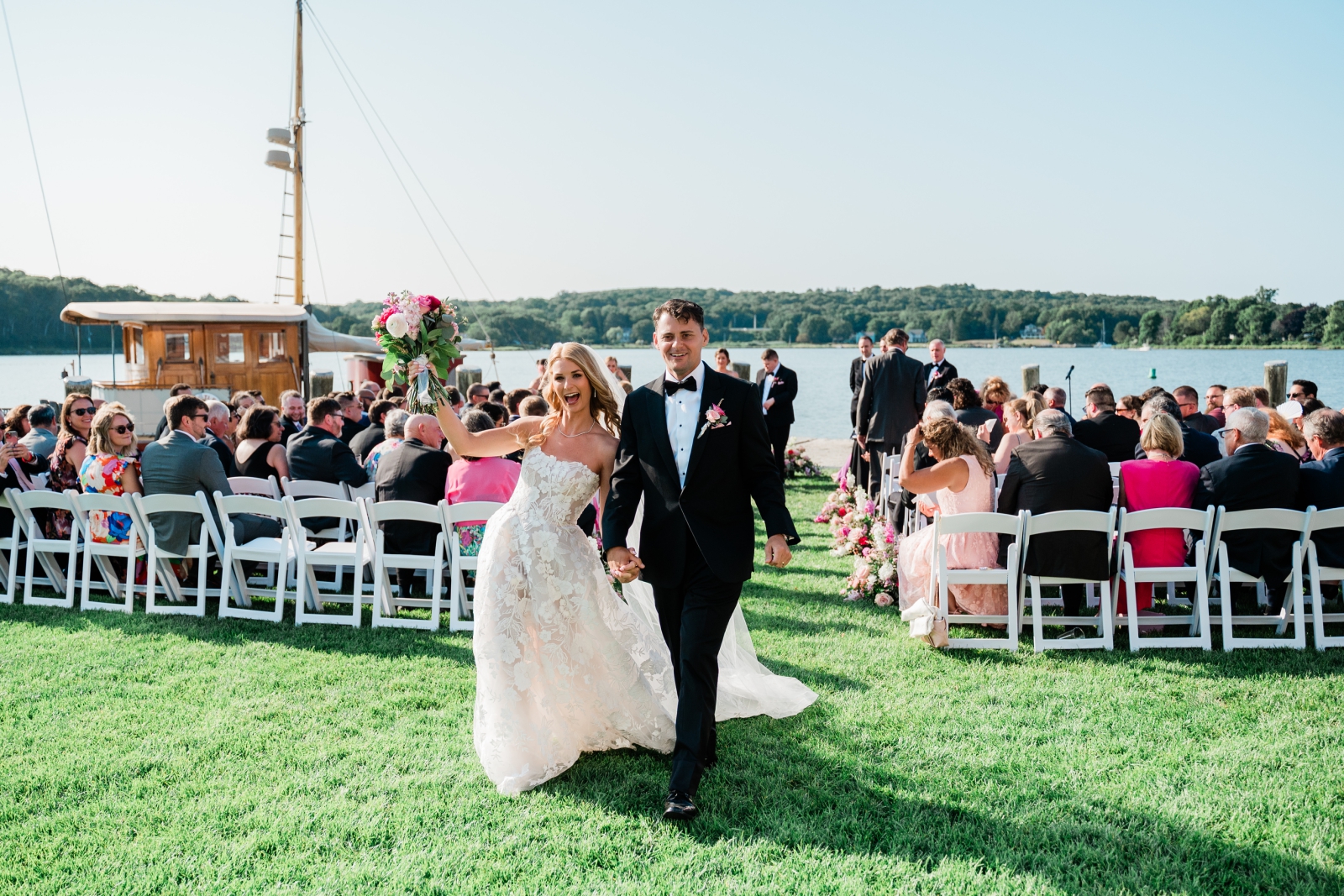 A bride and groom walk back up their wedding aisle with the Mystic River in the background