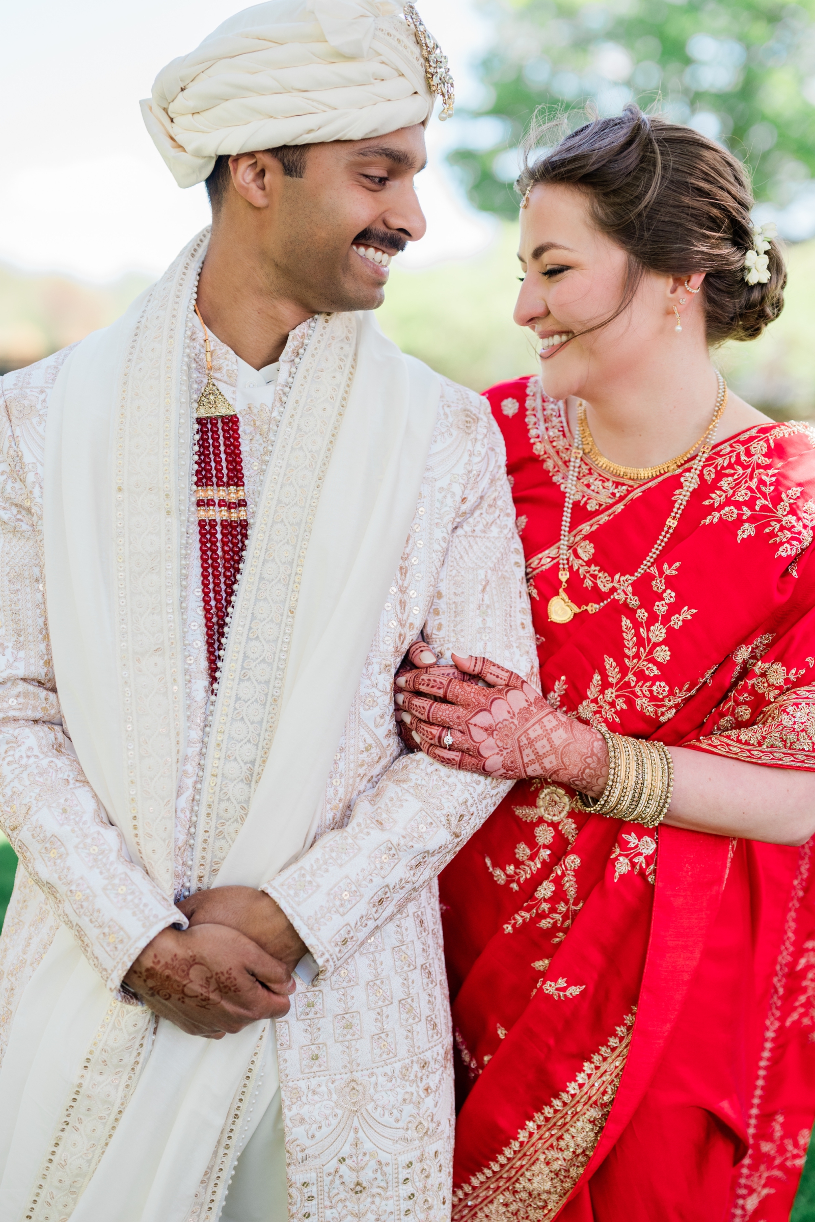 A portrait of a bride in a red saree and a groom in a white sherwani during an American Indian Wedding