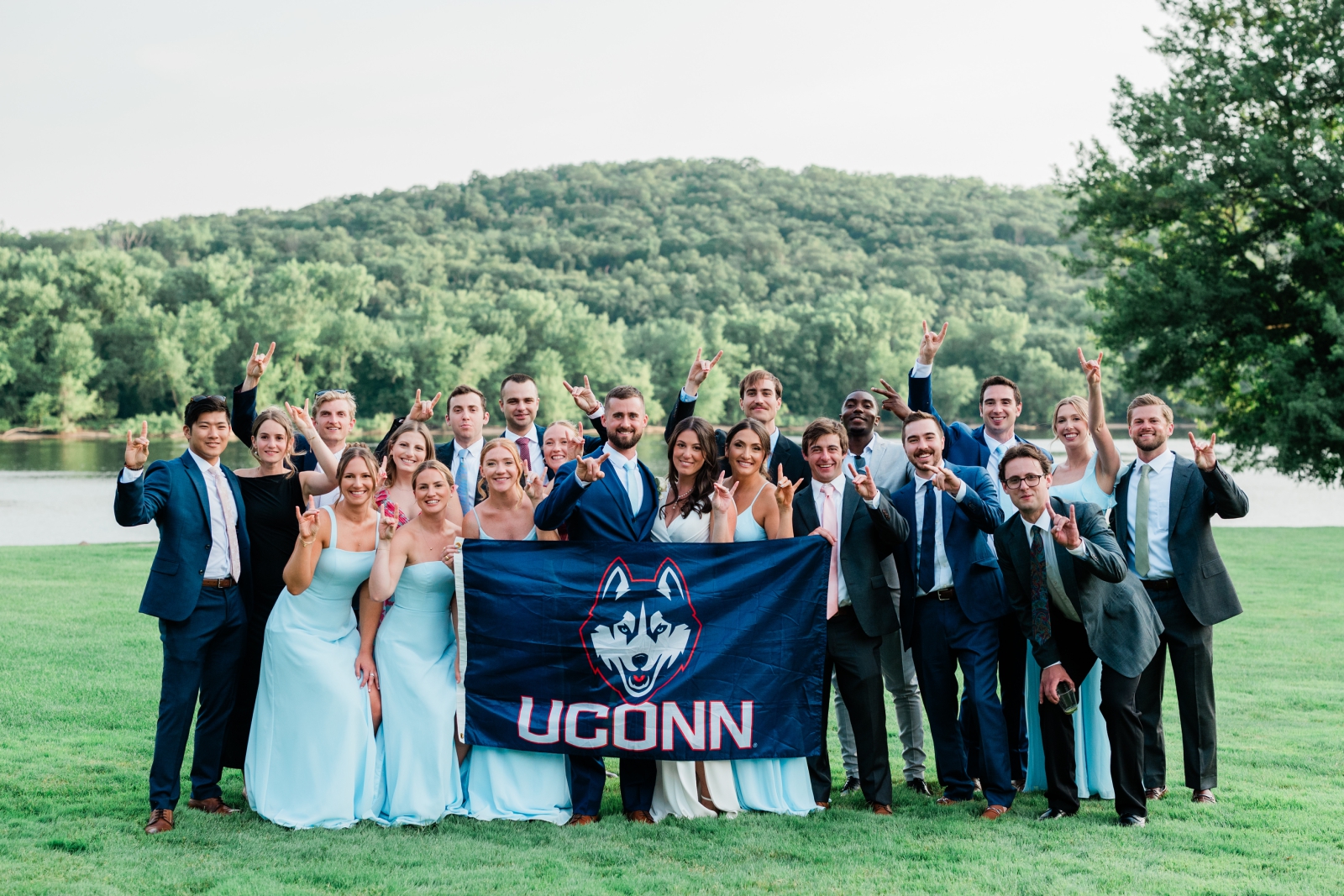 A bride, groom, and their guests stand behind a UConn Huskies flag