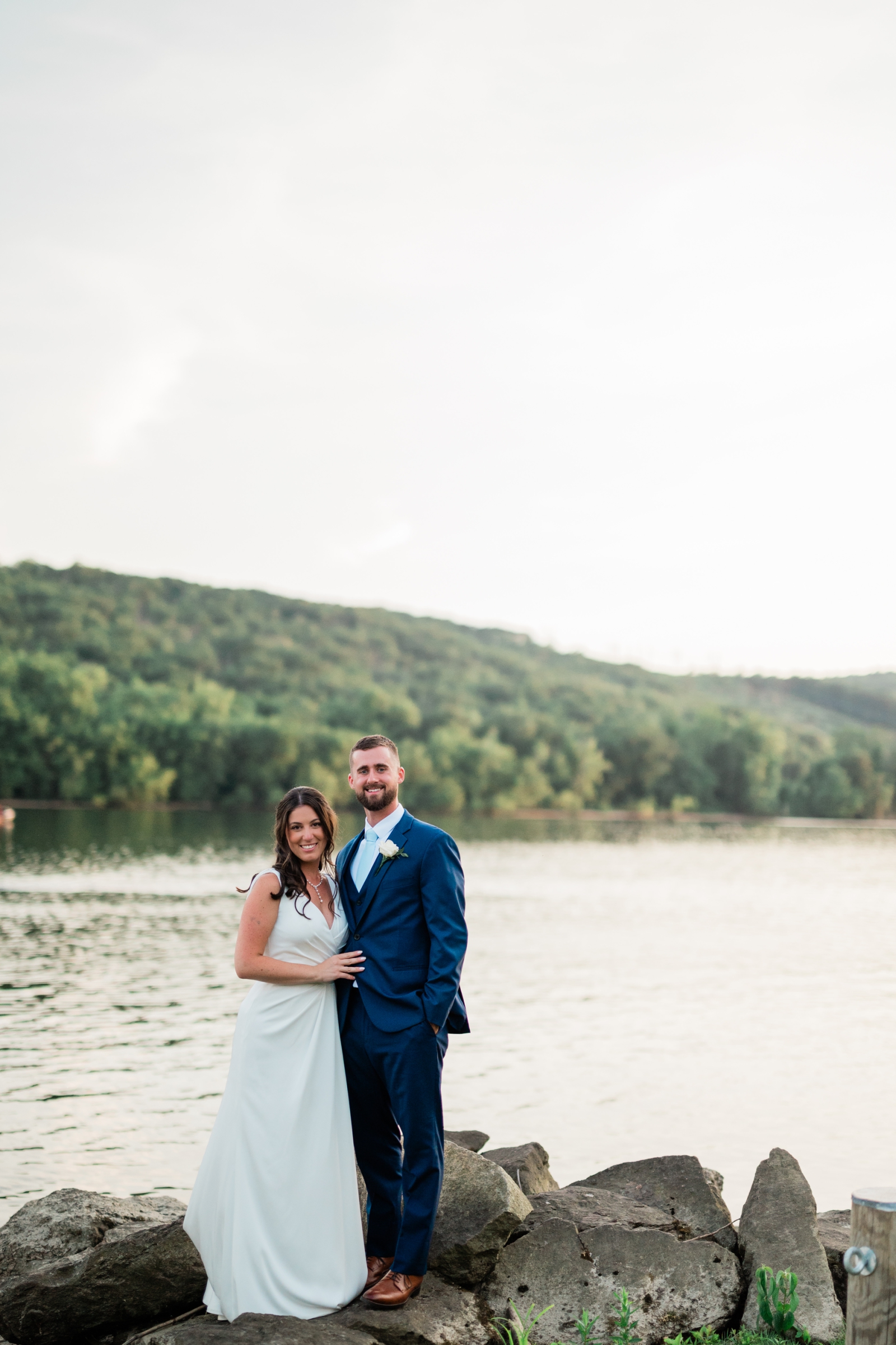 A bride and groom stand on the rocky shore of the Connecticut River at Saint Clements Castle