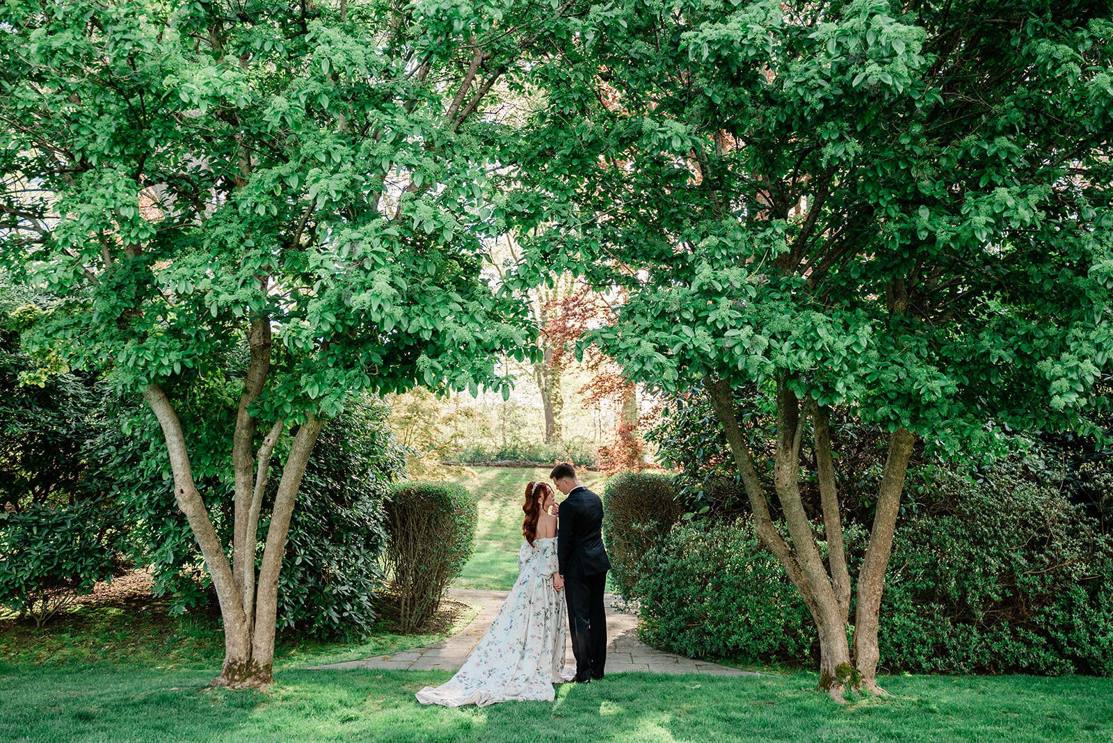 A bride and groom stand beneath the greenery in the garden at Glen Manor House
